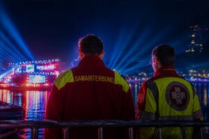 Samariterbund-Mitarbeiter blicken auf beleuchtete Donau und Linz bei Nacht